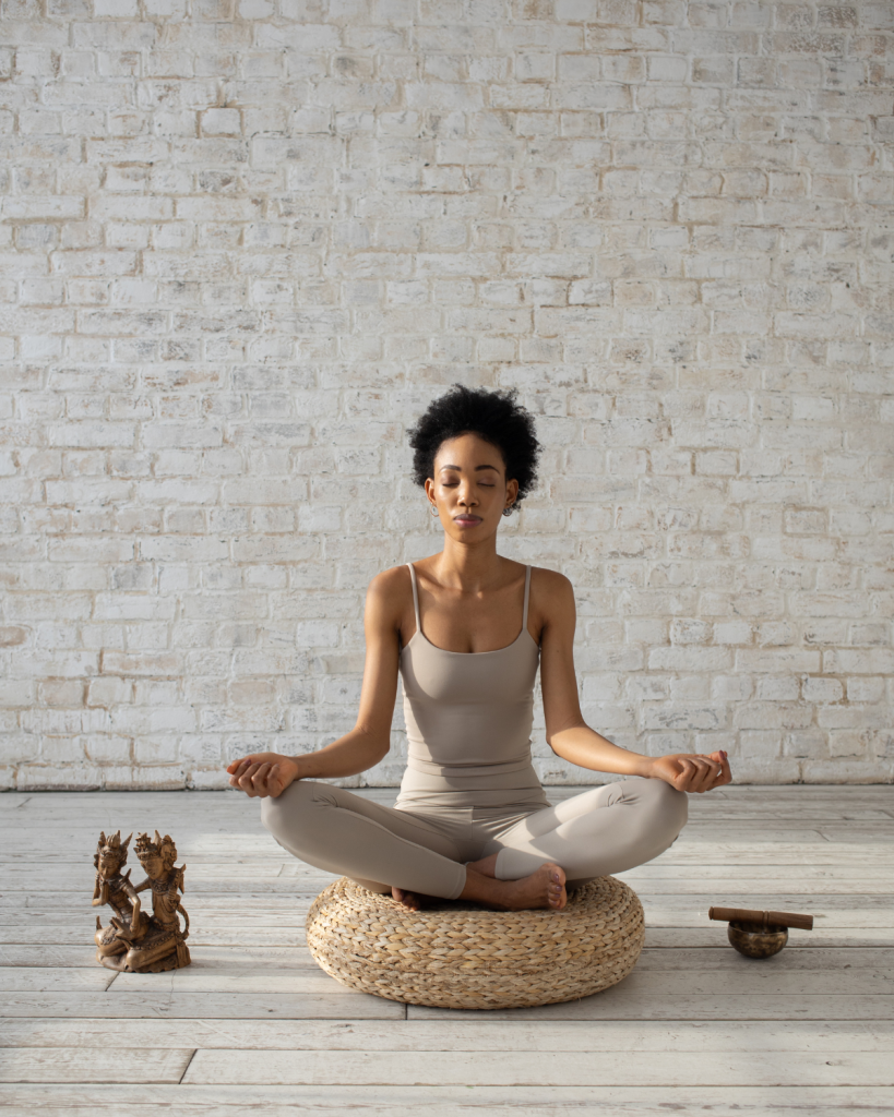Woman meditating in a white room, sitting on a meditation pillow. 