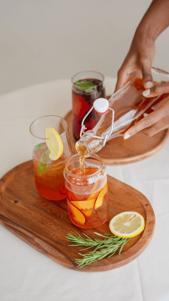 hands pouring juice into glassware that has fresh fruit in it.